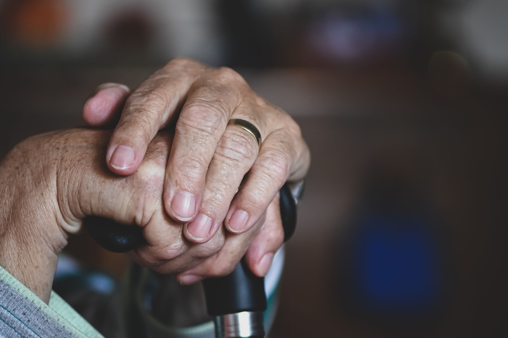 A caregiver's hand resting gently on an older adult's hand holding a cane
